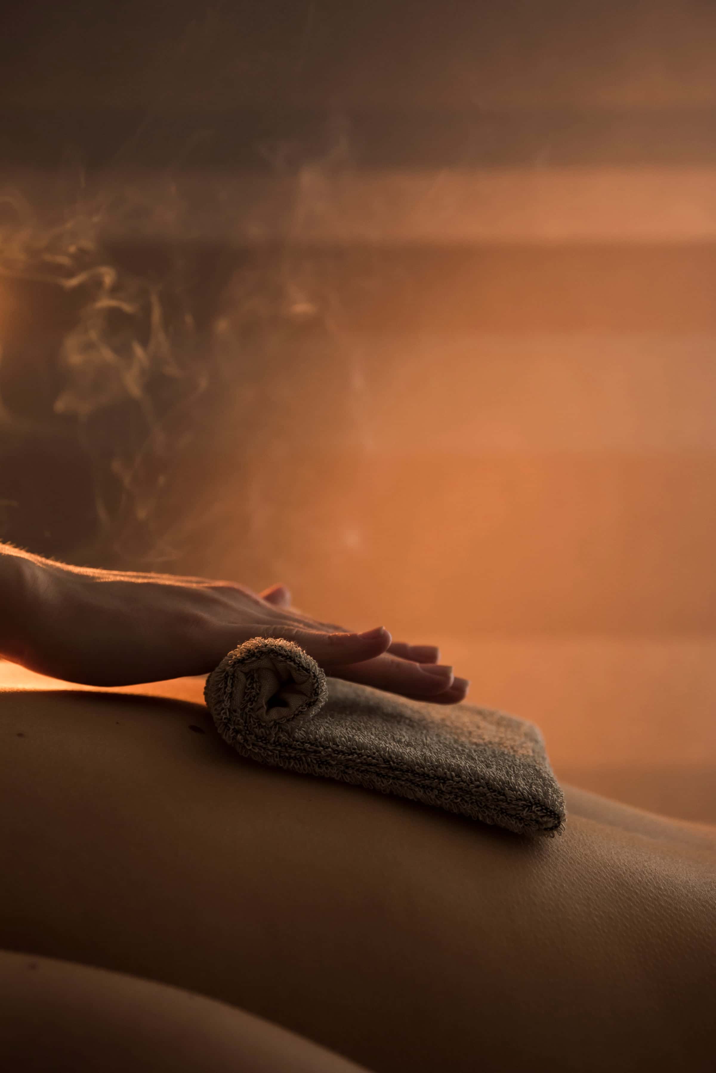 Hand placing a warm, steaming cloth on a back, warm backlight