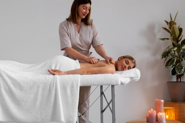 Therapeutin massiert die Schultern einer Frau auf einer mobilen Massageliege