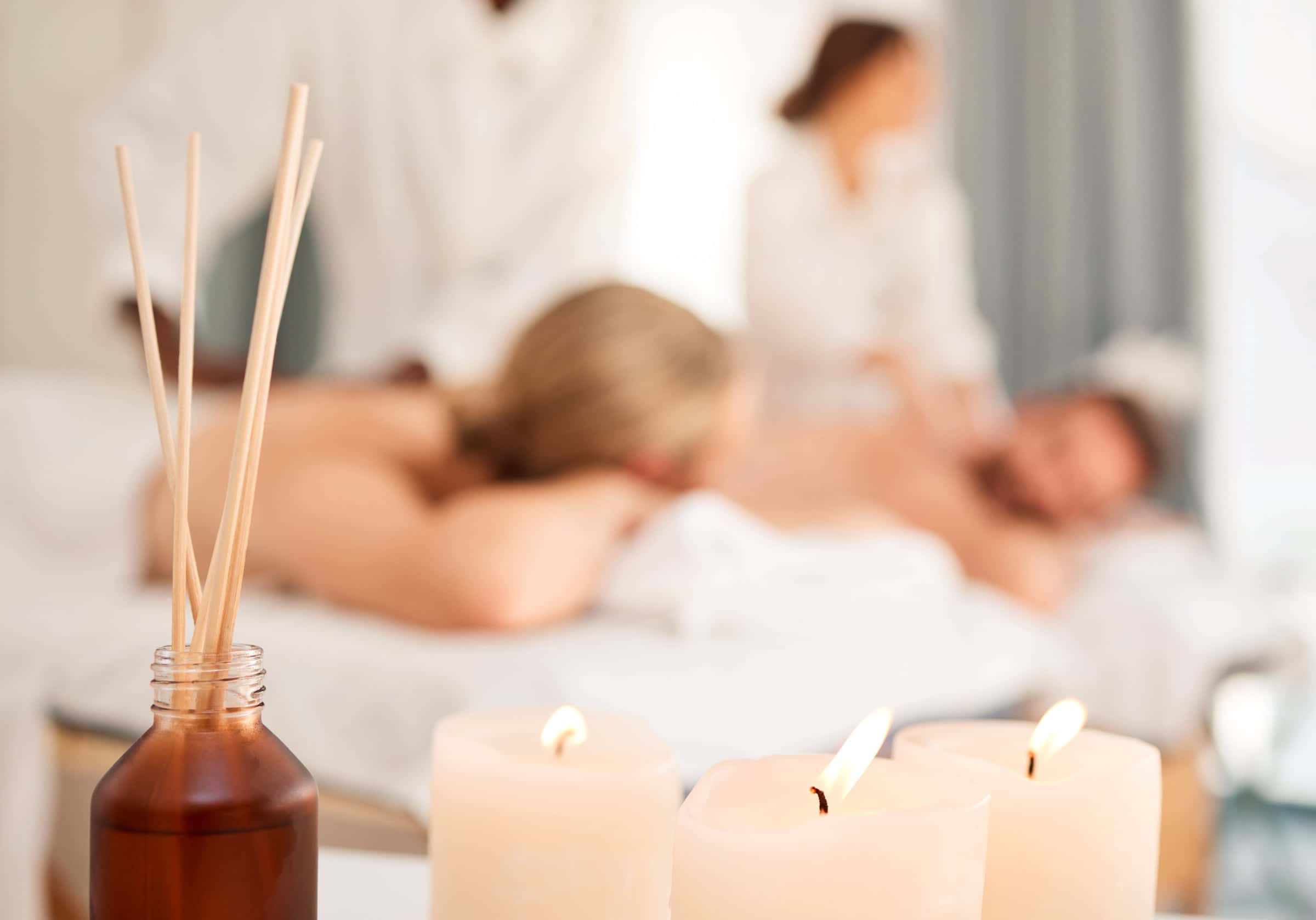 Paar bei einer gemeinsamen Massage, im Vordergrund Kerzen und ein Duftstäbchen-Flakon